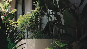 Un espacio exterior bien cuidado con diversas plantas, una jardinera de concreto y una estructura con techo de paja.