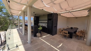 An outdoor patio with a dining table and chairs, a kitchen area, and a large potted plant. - Douze Boutique Hotel (Pecatu)