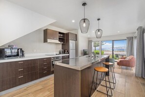 A modern kitchen with a central island, bar stools, and a view of the outdoors. - Soleil by the Sea (Whitianga)