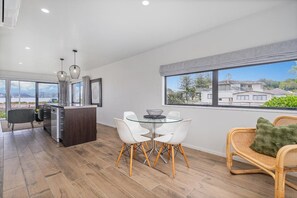 A modern kitchen with a dining area, large windows, and a view of the surrounding area. - Soleil by the Sea (Whitianga)