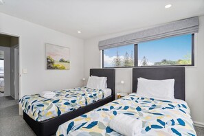 A hotel room with two beds, a painting on the wall, and a window with a view of trees. - Soleil by the Sea (Whitianga)
