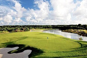 Ein Golfplatz mit einem Wasserhindernis und Bäumen im Hintergrund.