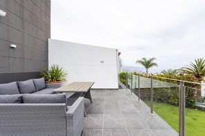 Eine moderne Außenpatio mit einer grauen Couch, Korbmöbeln und Blick auf die Stadtlandschaft.