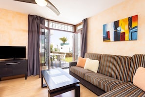 A modern living room with a flat-screen TV, a sofa with striped cushions, a coffee table, and a painting on the wall. - Cozy apartment with a terrace and pool in sunny southern Tenerife (Costa Adeje)