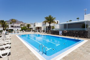 A swimming pool with lounge chairs and a stone wall. - Cozy apartment with a terrace and pool in sunny southern Tenerife (Costa Adeje)