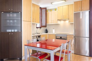 A modern kitchen with wooden cabinets, a stainless steel refrigerator, and a red table with chairs. - Cozy apartment with a terrace and pool in sunny southern Tenerife (Costa Adeje)