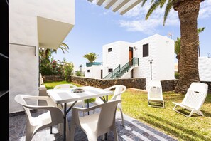 Um pátio com mesa e cadeiras, um muro de pedra e uma escadaria que leva a um edifício branco.