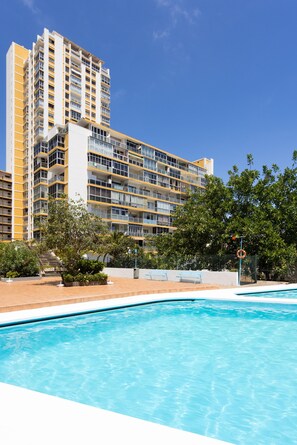 Ein modernes Hotel mit Schwimmbad, mehreren Balkonen und üppiger Bepflanzung.