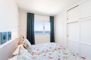 Een slaapkamer met een bed, een raam met gordijnen, een kledingkast en een wandlamp.