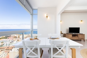 Ein moderner Essbereich mit Tisch und Stühlen, einem Fernseher und Blick auf Stadt und Meer.