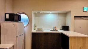 A compact kitchenette with a microwave, refrigerator, sink, and a small window. - JIA Kamei Osaka (Osaka)