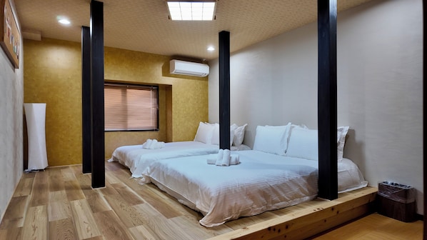 A hotel room with two beds, a wooden floor, a window with blinds, an air conditioning unit, and a trash bin. - JIA Kamei Osaka (Osaka)