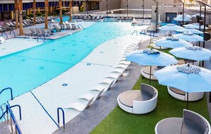 En swimmingpool med liggestole og parasoller, omgivet af en bygning.