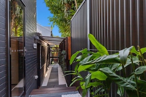 A narrow outdoor corridor with a wooden walkway, metal railing, and lush green plants. - The Douglas House | 3BR Spring Hill Escape (Spring Hill)