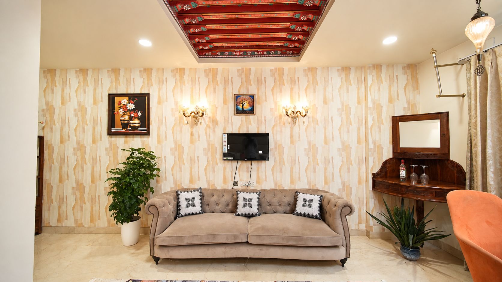 A living room with a sofa, a television, wall-mounted lights, a mirror, and a potted plant.