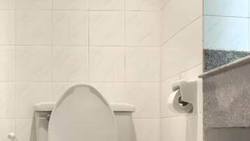 A bathroom with a toilet, a hand dryer, and a trash bin.