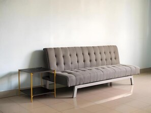 A modern sofa with a tufted backrest and a matching ottoman, positioned against a plain wall with a tiled floor. - Cloudy B Chidlom (Krung Thep Maha Nakhon)