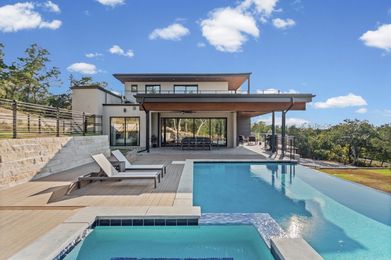 Una casa moderna con piscina, mobiliario exterior y un patio cubierto.