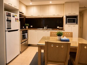 Eine moderne Küche mit Kühlschrank, Backofen, Mikrowelle und einem Holzessttisch mit Stühlen.