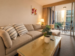 Ein Hotelzimmer mit einer Couch, einem Glastisch, einem Blumentopf, einer Lampe und Blick auf den Balkon.