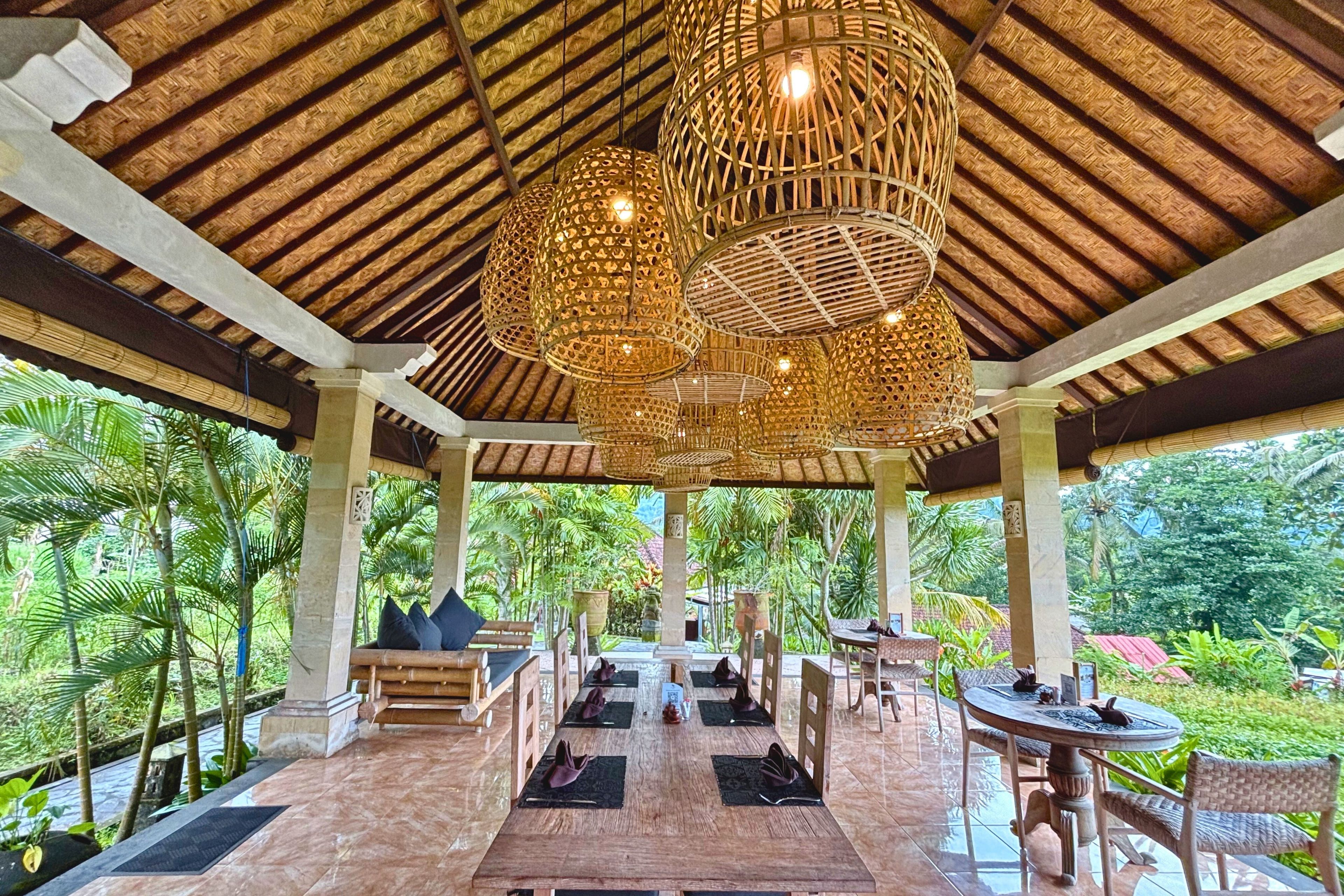 Un área de comedor al aire libre con techo de paja, mobiliario de madera y vista a exuberante vegetación.