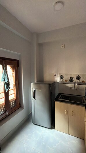A compact kitchen with a refrigerator, a sink, and a window with a towel hanging. - Traditional 3-Bedroom Apartment Near Patan Square (Lalitpur)