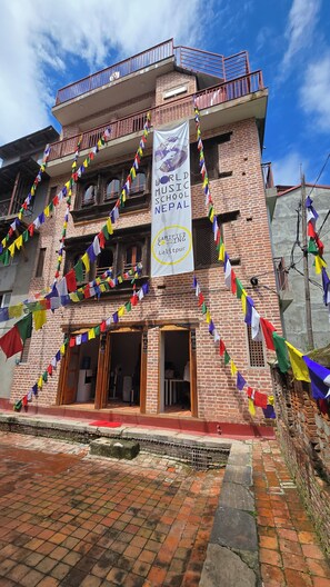 A building with a banner reading 'World Music School Nepal' and multiple balconies with colorful prayer flags. - Traditional 3-Bedroom Apartment Near Patan Square (Lalitpur)