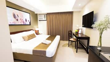 A hotel room with a bed, a desk, a chair, a television, and a window with curtains.