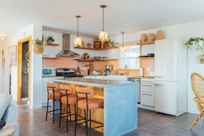 Una cocina moderna con una isla central, taburetes de bar, un refrigerador y lámparas colgantes.