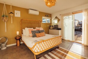 A bedroom with a bed, bedside tables, a lamp, a hanging plant, and a view of the outdoors. - Pool, Hot Tub & Sauna - 5 Min to Joshua Tree NP & Downtown- Epic Views (Joshua Tree)