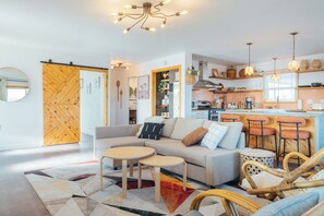 A modern living room with a sofa, coffee table, and chairs, a kitchen with bar stools, and a dining area with a table and chairs. - Pool, Hot Tub & Sauna - 5 Min to Joshua Tree NP & Downtown- Epic Views (Joshua Tree)