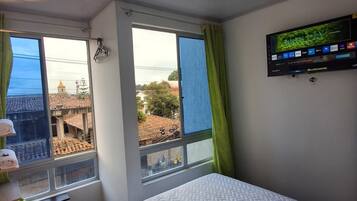 Une chambre d’hôtel avec un lit, un téléviseur fixé au mur et une fenêtre avec des rideaux.