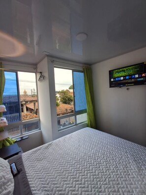 Une chambre d’hôtel avec un lit, un téléviseur fixé au mur et une fenêtre avec des rideaux.