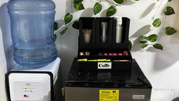 Een koffieapparaat en een waterdispenser in een ruimte met een witte muur en groene planten.