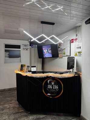 Een receptiebalie met een beeldscherm, een bord waarop 'ZIG ZAG' staat en diverse mededelingen aan de muur.