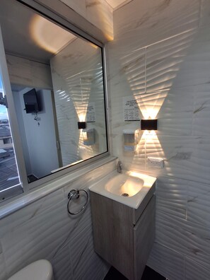 Een badkamer met een grote spiegel, een wastafel en een toilet. Er zijn wandlampen en een raam.