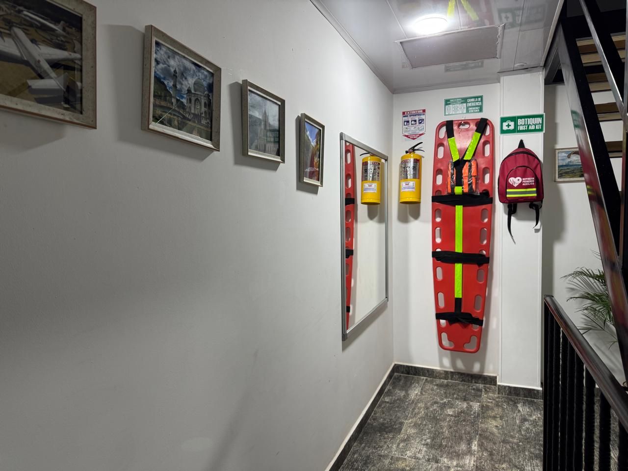 Un pasillo con cuadros en la pared, un chaleco salvavidas rojo y un cartel que indica botiquín de primeros auxilios.