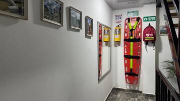 Un pasillo con cuadros en la pared, un chaleco salvavidas rojo y un cartel que indica botiquín de primeros auxilios.