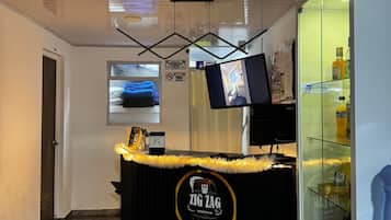 Un área de recepción con mostrador, un televisor montado en la pared y un expositor de vidrio con bebidas.