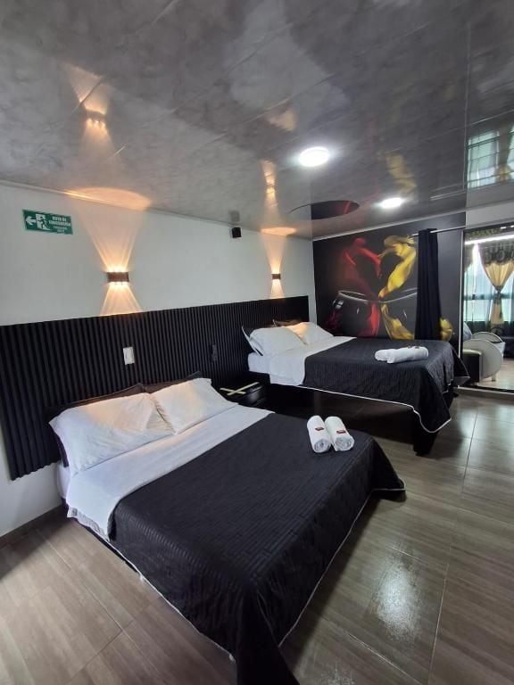 A hotel room with two beds, each with a black bedspread and white pillows, a wooden floor, and a wall-mounted light fixture.