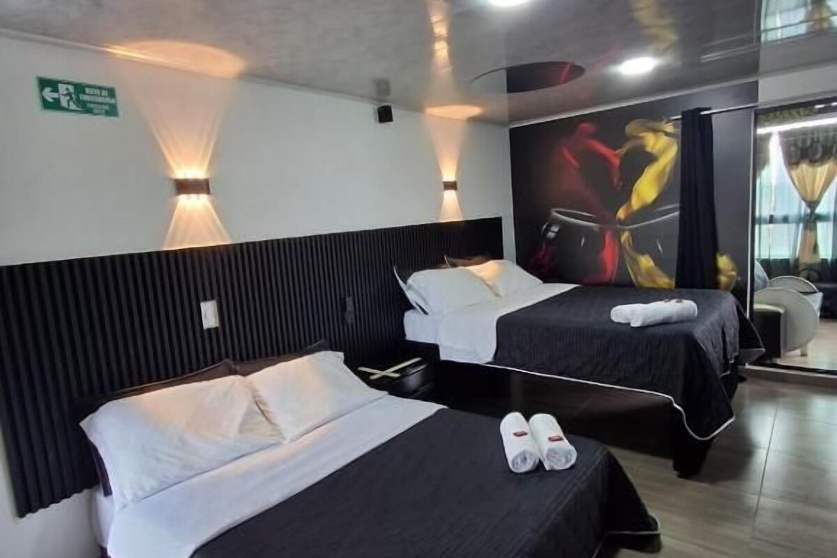 Een hotelkamer met twee bedden, elk met een zwart sprei en witte kussens, een houten vloer en een wandlamp.