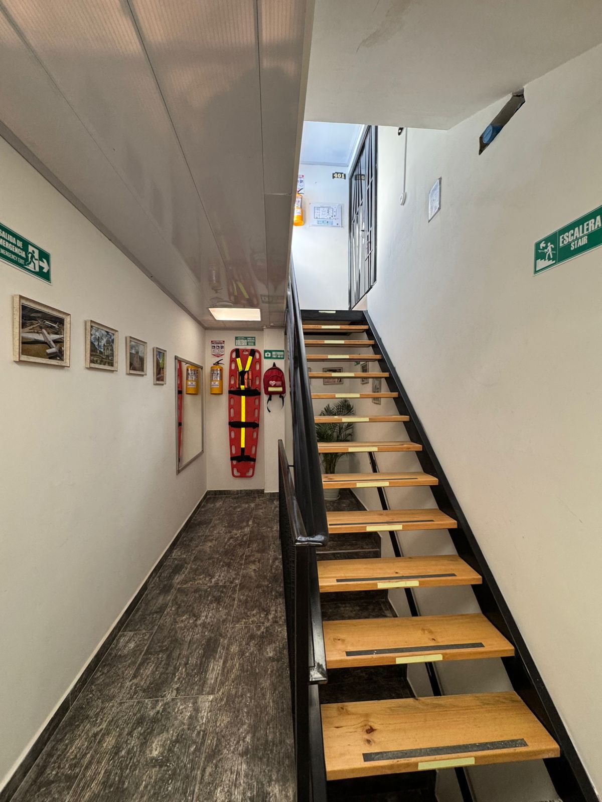Een wenteltrap met houten leuning, pictogrammen voor vluchtweg en afbeeldingen in lijsten aan de wand.