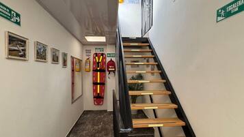 Een wenteltrap met houten leuning, pictogrammen voor vluchtweg en afbeeldingen in lijsten aan de wand.