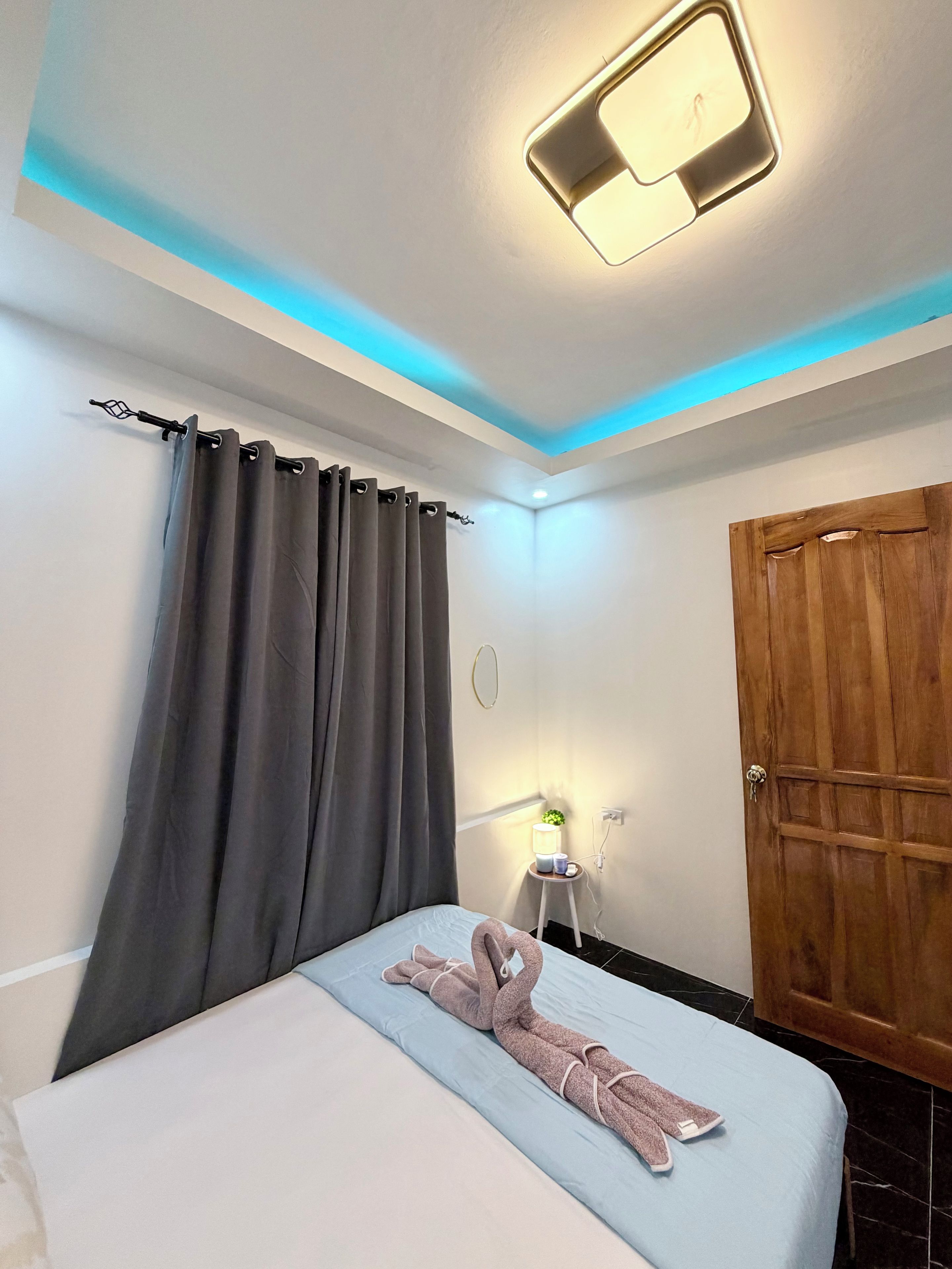Une chambre d’hôtel avec un lit, une porte en bois, une table de chevet avec une lampe et un luminaire au plafond.