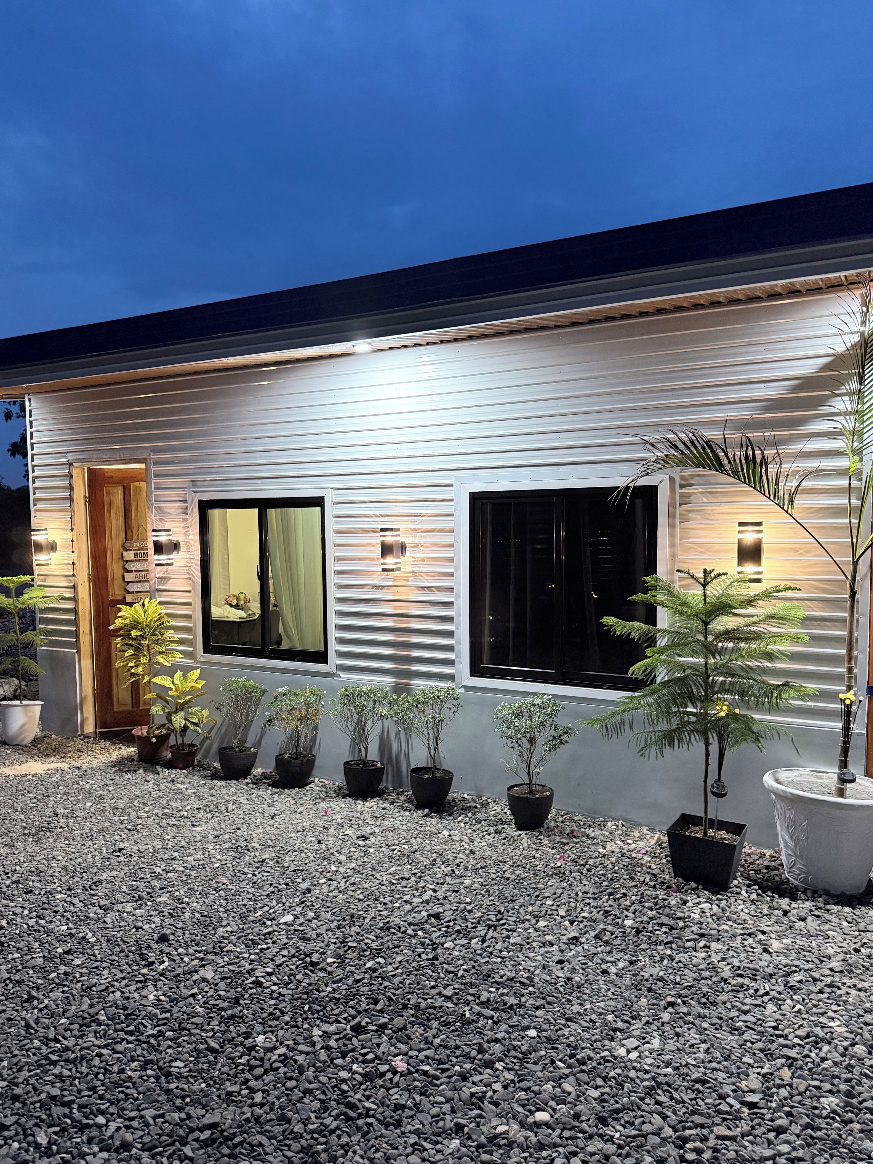 Una casa moderna con camino de grava, plantas en macetas y una puerta de madera.