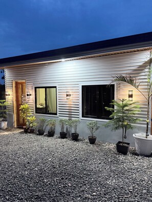 Una casa moderna amb un camí de grava, plantes en testos i una porta de fusta.