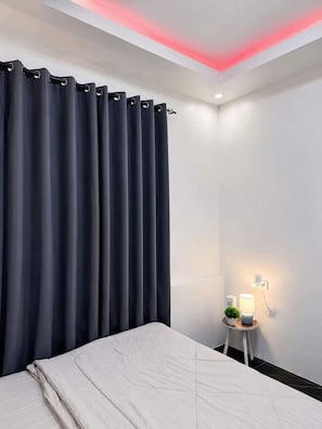 Un dormitori amb un llit, una taula de nit, una làmpada i una finestra amb cortines.