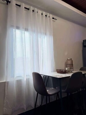 A dining area with a table, chairs, and a window with sheer curtains.