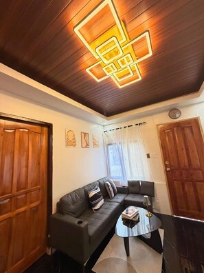 A modern living room with a sectional sofa, a coffee table, and a wooden ceiling with geometric light fixtures.