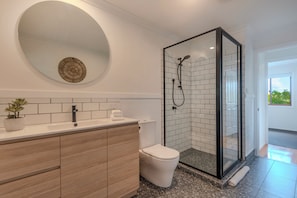 Un baño moderno con cabina de ducha de vidrio, un espejo redondo y un tocador de madera.